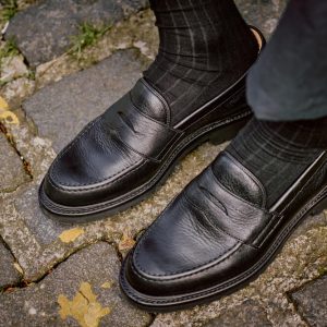 Men's loafer outfit ideas for the fashion-forward gentleman. Man wearing black leather loafers with socks on cobbles.