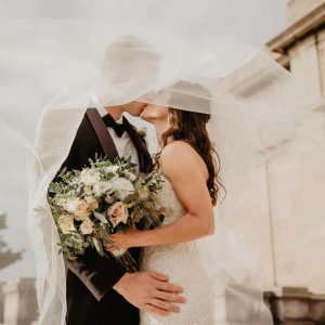 Men's wedding tuxedo shoes. Bride and groom kissing under a wedding veil. Bride is holding a blush bouquet.