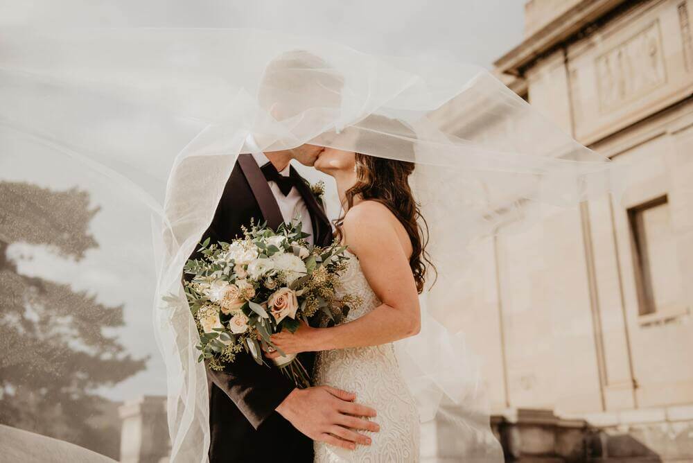 Men's wedding tuxedo shoes. Bride and groom kissing under a wedding veil. Bride is holding a blush bouquet.